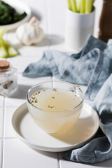 Healthy golden bone broth with spices in a mug on a saucer on a white background. The concept of paleo and keto diets.