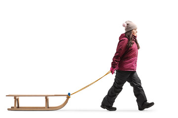 Full length profile shot of a girl in winter clothes walking and pulling a sled