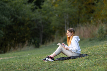 A young woman writes a letter in the park on the grass