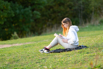 A young woman is sitting in a park and writing in a notebook