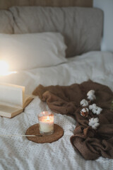 Cozy still life interior details with a book, candle and a cotton twig in warm soft bed. Sweet home