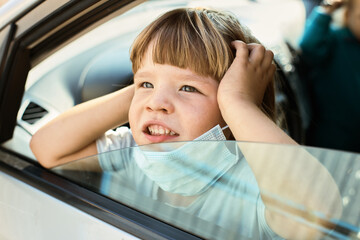 Child sits in the car holding a mask and looks away from the window