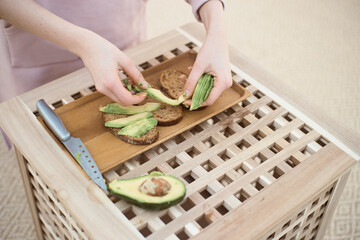 Wide angle of young woman puts the slice of avocado on the bread