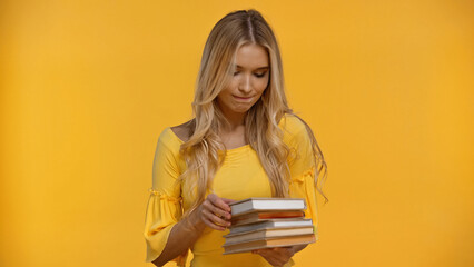 Pensive blonde woman holding books isolated on yellow.