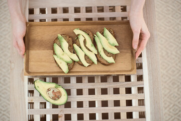 Top view of woman hands holds the wooden tray with toasts with avocado