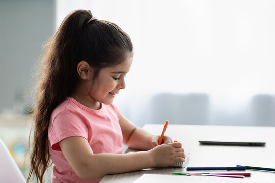 Profile Shot Of Little Smiling Girl Drawing With Colorful Pencils At Home