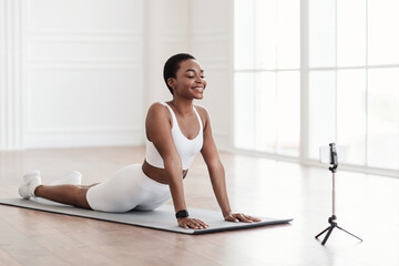 Young african woman stretching back on mat with cellphone