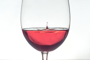 Wine drop falls into rose wine glass on white background.