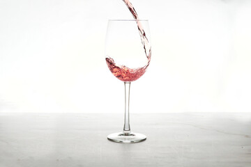 Rose wine is pouring into a glass goblet on a white background.