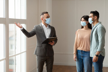 Real Estate Agent In Facemask Showing Young Buyers New Property