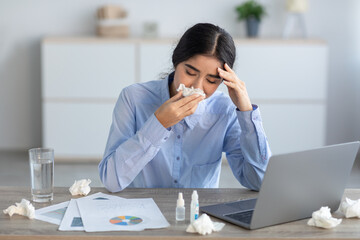Sad millennial hindu woman manager sick, blows nose in napkin, suffers from headache, cold in office interior