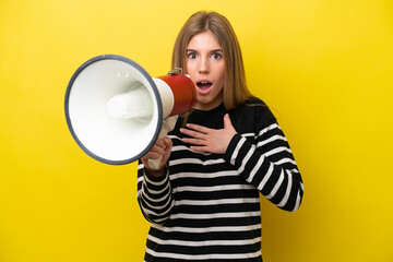 Young caucasian woman isolated on yellow background shouting through a megaphone with surprised expression