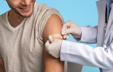 Doctor Applying Sticking Plaster On Young Man's Shoulder After Vaccine Injection Shot - obrazy, fototapety, plakaty