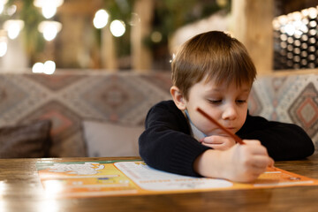 cute little boy drawing with colour pencils sitting at the table in restaurant