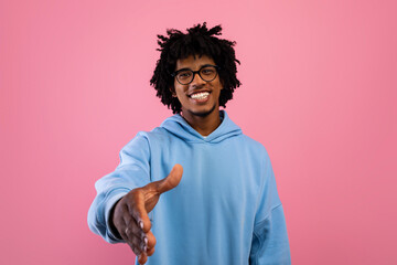 Smiling black teenager offering handshake greeting on pink studio background. Partnership, deal or agreement concept © Prostock-studio
