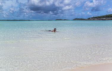 Beautiful view of man floating in Atlantic ocean on sandbar with white sand at low tide in Bahamas islands. 