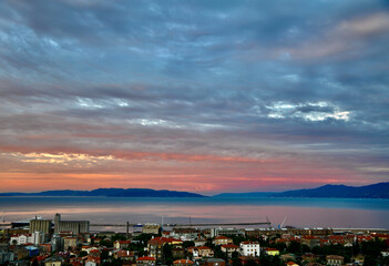 Fototapeta na wymiar Sky covered with clouds and rijeka gulf in pink summer sunset. Sunset over the city.