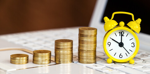 Gold coins and alarm clock on a laptop. Money savings, inflation, online investment banner.