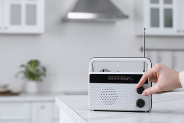 Woman turning volume knob on radio in kitchen, closeup. Space for text