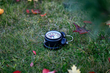 the black alarm clock is lying on the green grass among the autumn leaves