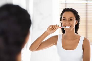 Happy Young Middle Eastern Woman Brushing Her Teeth With Toothbrush In Bathroom