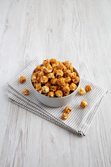 Homemade Caramel Popcorn in a gray Bowl on a white wooden background, side view.