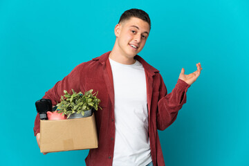 Young caucasian man making a move while picking up a box full of things isolated on blue background...