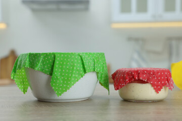 Bowls covered with beeswax food wraps on wooden table in kitchen