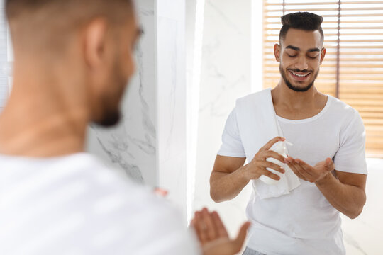 Men Skincare. Handsome Young Arab Man Using Aftershave Lotion In Bathroom