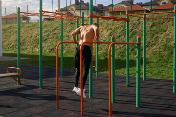 Back view of shirtless caucasian man exercising on parallel bars outdoors. Strong male athlete...
