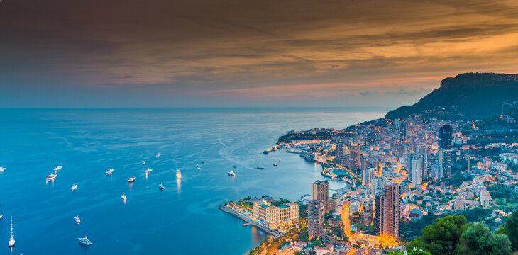 A lot of yachts and motor boats with night illumination are moored in mediterranean sea, aerial view of bay of Monaco - Monte-Carlo at dusk, cityscape with night illumination