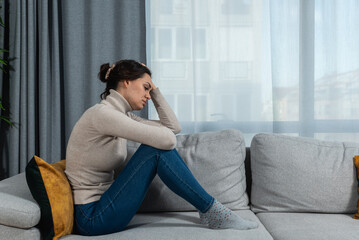 Young sad woman with broken heart sitting alone at home suffering from depression anxiety and bad mental condition. Female having hard time and burnout of overthinking and worry  - obrazy, fototapety, plakaty