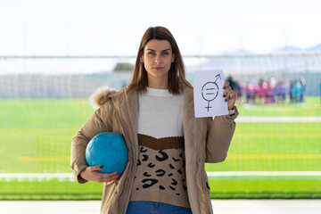 Close-up of a young woman holding a soccer ball and a paper with a symbol of gender equality drawn...