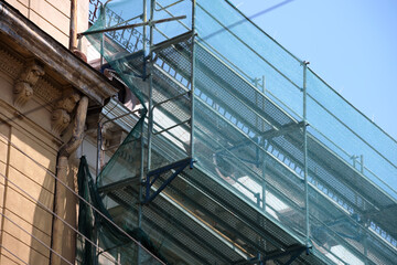 Building facade under renovation works with construction scaffolding frame covered with protective net for workers safety