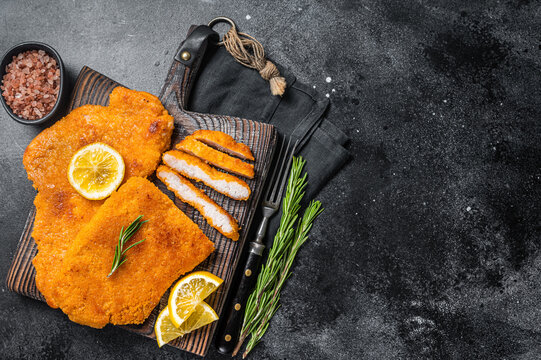 Fried sliced weiner schnitzel on a wooden board with herbs. Black background. Top view. Copy space