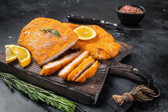 Fried sliced weiner schnitzel on a wooden board with herbs. Black background. Top view