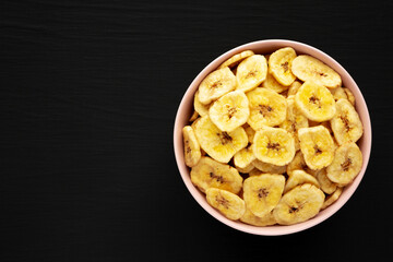 Homemade Banana Chips in a Pink Bowl on a black background, top view. Flat lay, overhead, from above. Space for text.