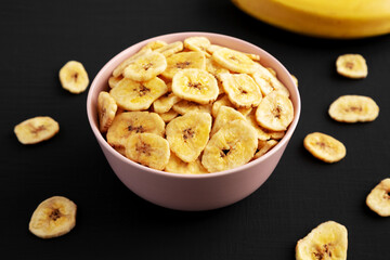 Homemade Banana Chips in a Pink Bowl on a black background, low angle view.