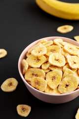Homemade Banana Chips in a Pink Bowl on a black background, low angle view.