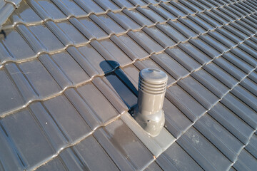 Closeup of ventilation pipe on house roof top covered with ceramic shingles. Tiled covering of...