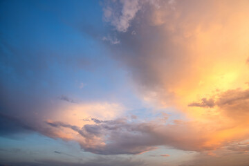 Dramatic sky at sunset with puffy clouds lit by orange setting sun