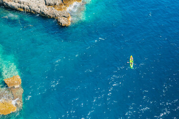 Fototapeta na wymiar Top view of sportsmen or tourists kayaking in the turquoise transparent blue water of Adriatic sea rocky shore. Summer leisure activity in the canoe. 