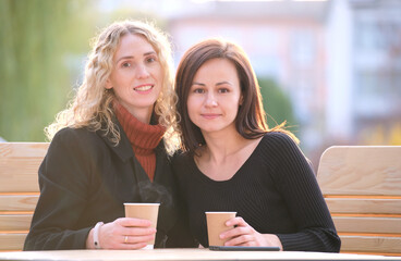 Happy young women friends drinking coffee at city street restaurant during work break. Socializing and friendship concept