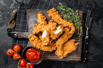 Dip fried Breaded chicken breast strips with tomato ketchup on a wooden board. Black backgrund. Top...