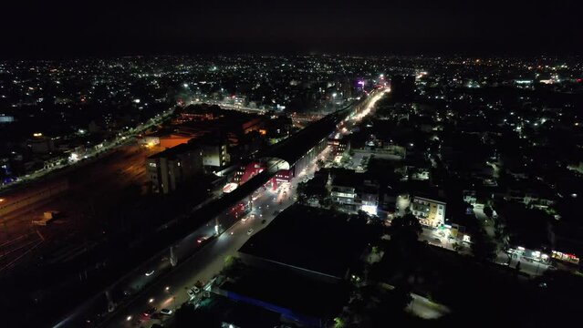 aerial drone shot at night orbiting elevated metro station with train and a busy street underneath in jaipur rajasthan india