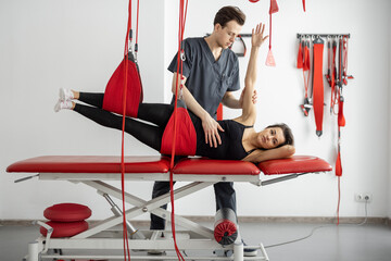 Rehabilitation specialist doing active treatment on suspension straps to female patient. Concept of...