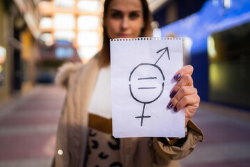 A young woman holds a paper with a gender equality symbol drawn.