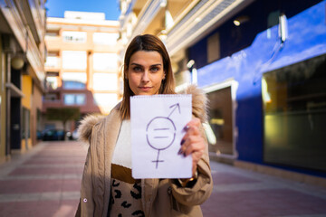 A young woman holds a paper with a gender equality symbol drawn. The focus is on the woman's face.