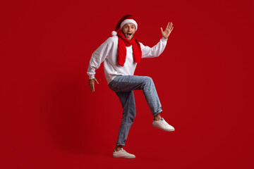 Christmas Dance. Funny Guy In Santa Hat Dancing Over Red Studio Background