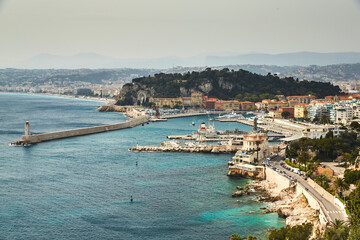 The ferry terminal in port Nice - France at sunny day, A lot o motor boats and luxury yachts are moored in port, mooring ropes go into the amazing azure water, famous embankment and lighthouse